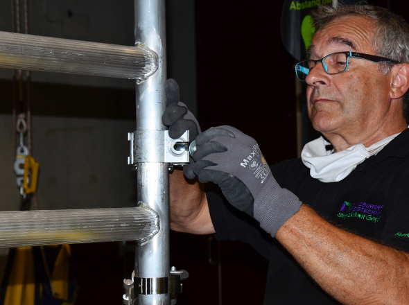 Mann befestigt Gerüstteile mit einer Metallschelle