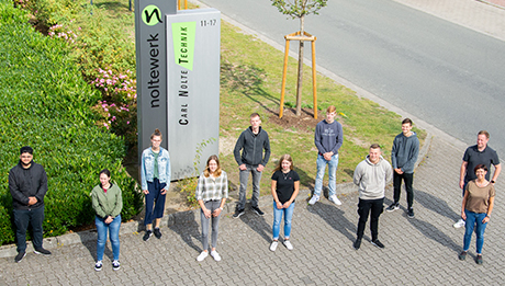 Herzlich Willkommen unseren neuen Azubis Neun Auszubildende und zwei Ausbildungsverantwortliche stehen auf einer Parkplatzeinfahrt vor den Logos der Firmen Carl Nolte Technik und noltewerk