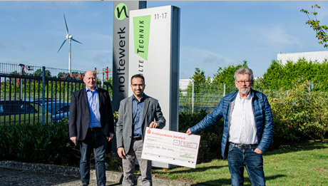 Rami Awad übergab im Namen des nolteteams den Spendenscheck an den DRK Ortsverein Greven Drei Männer vor Firmenschildern mit großem Scheck bei einer Spendenübergabe