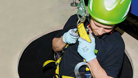 Grundkurs Confined Space (GK-CS) jetzt buchen! Höhensicherungs-Experte der Carl Nolte Technik mit grünem Helm wird in einen engen Raum abgelassen, Haken und Gurtband sind zu sehen