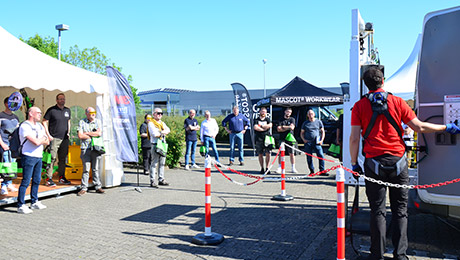 Zelte und Personen, die davor stehen. Rechts eine Absperrung vor einem Fahrzeug