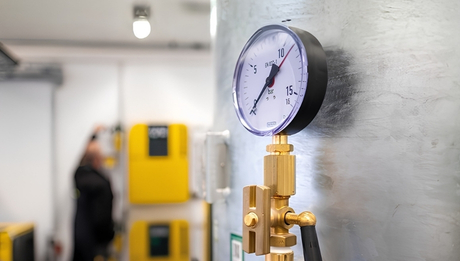 Nahaufnahme eines Druckluftmanometers mit Messskala von 0 bis 15 bar an einer metallischen Anlage