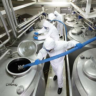 Personen in Schutzanzügen mit Atemschutzmasken befüllen Silotanks. Personen in Schutzanzügen mit Atemschutzmasken befüllen Silotanks.