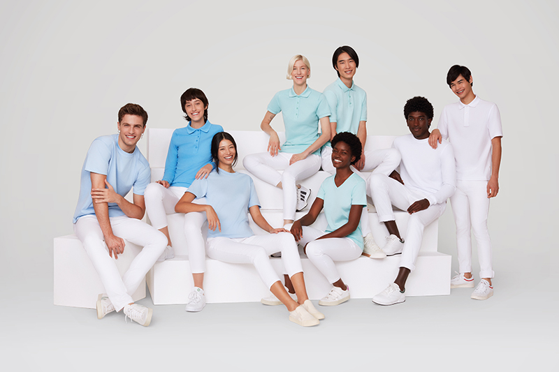 Gruppe von Personen aus dem Medizin-Umfeld mit typischen weißen und pastellfarbenen Bekleidungsstücken auf einer weißen Bank