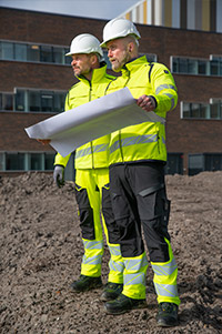 Zwei Männer in Warnschutzkleidung und Helmen mit einem Plan auf einer Baustelle.