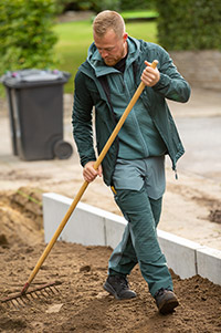 Mann in grüner Arbeitskleidung mit Rechen bei der Arbeit.