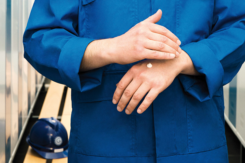 Detailansicht einer Person, Körpermitte und Arme, im Blaumann, Cremeklecks auf einer Hand