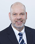 Portrait eines Mannes mit grauem Bart, Jackett und gestreifter Krawatte.